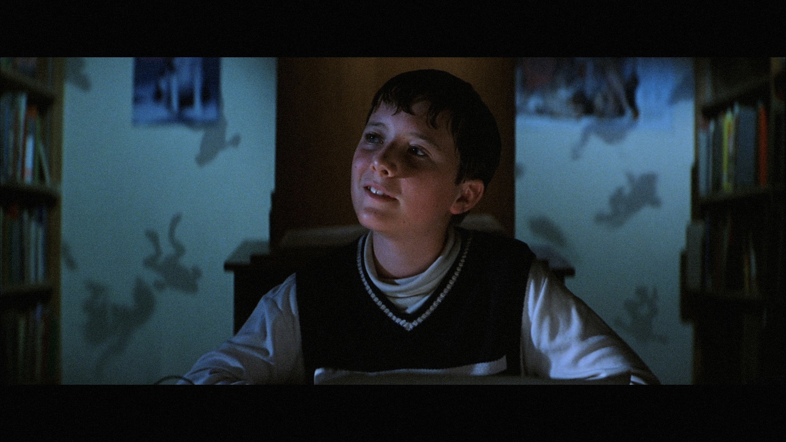 a young boy sitting in front of a book shelf