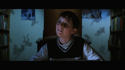 a young boy sitting in front of a book shelf