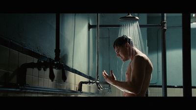 a shirtless man standing in a shower holding his hands out