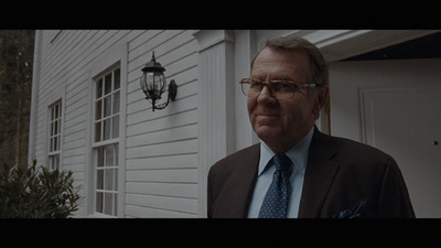 a man in a suit and tie standing in front of a house