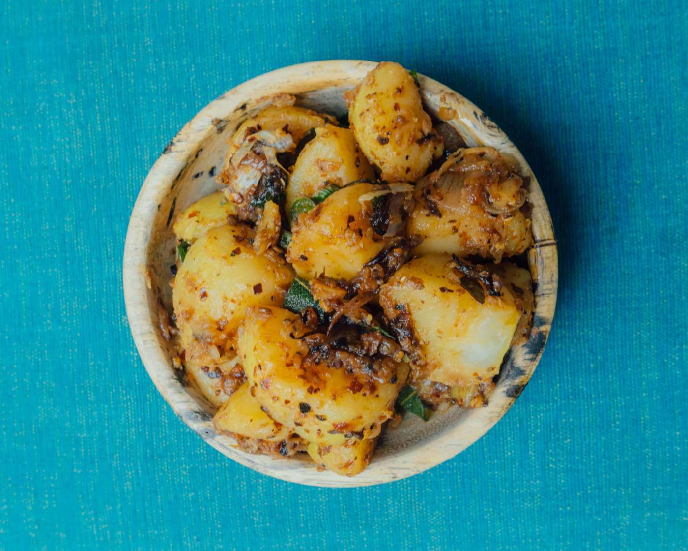 a wooden bowl filled with cooked potatoes on top of a blue table