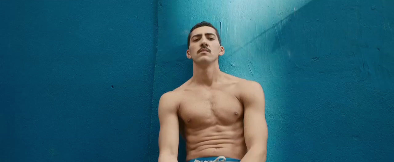 a shirtless man leaning against a blue wall