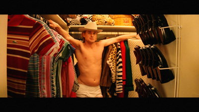 a shirtless man standing in front of a rack of clothes