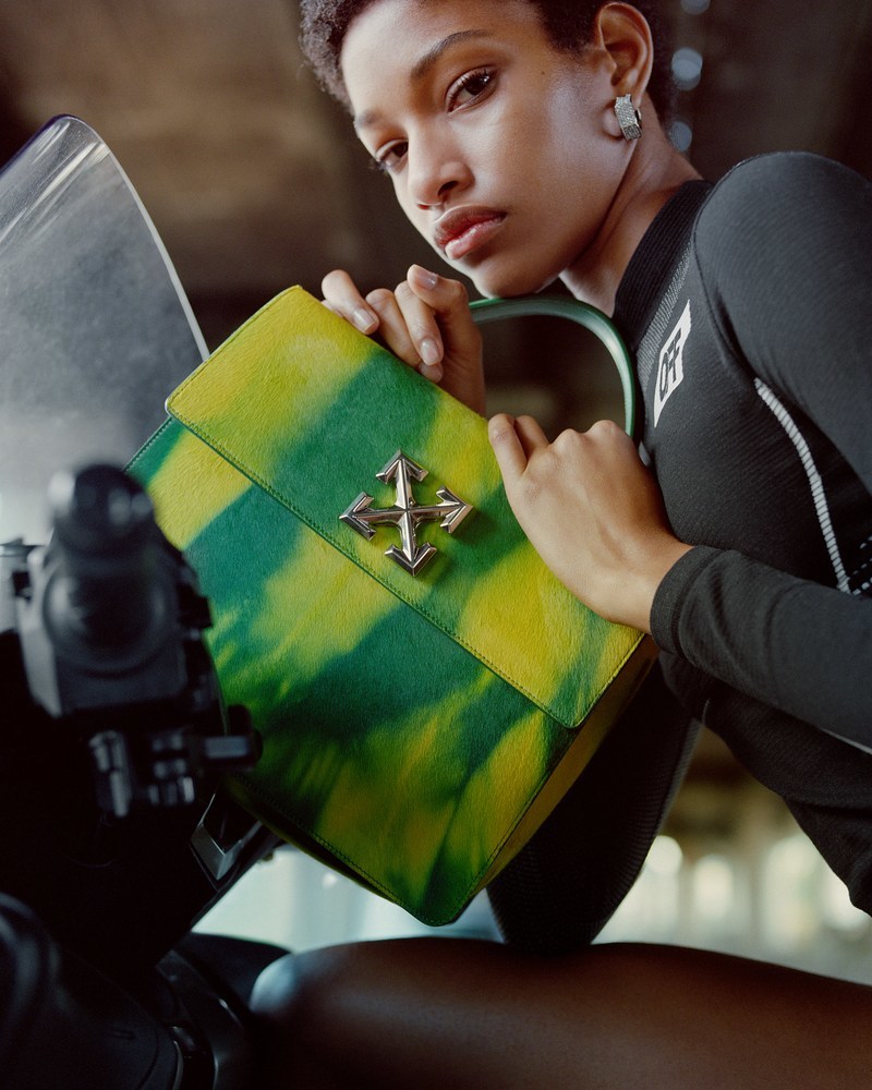 a woman sitting on a motorcycle holding a green bag