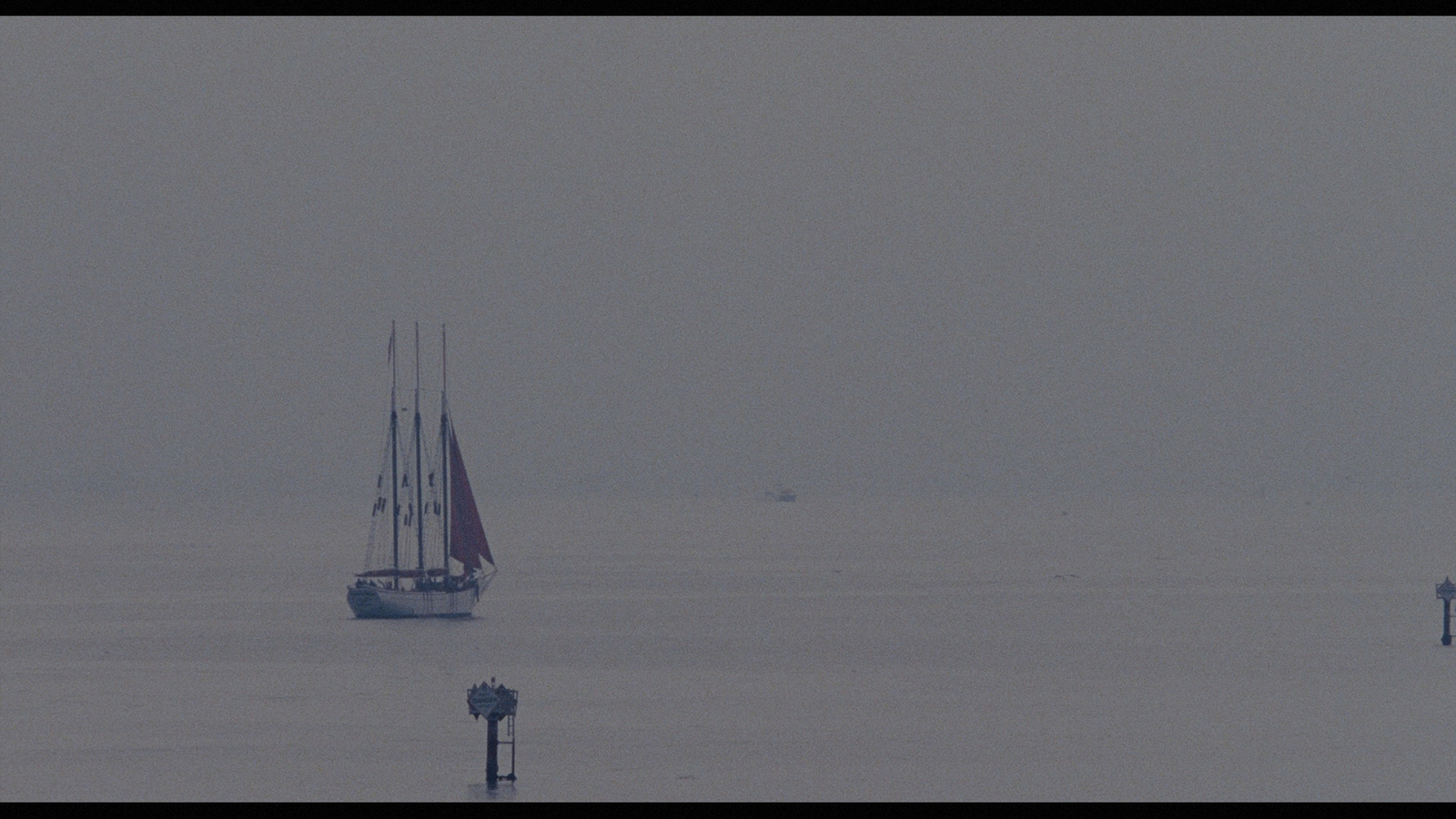 a sailboat in the middle of the ocean on a foggy day