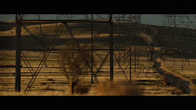 a man walking down a dirt road next to power lines