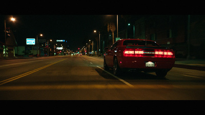 a red car driving down a street at night