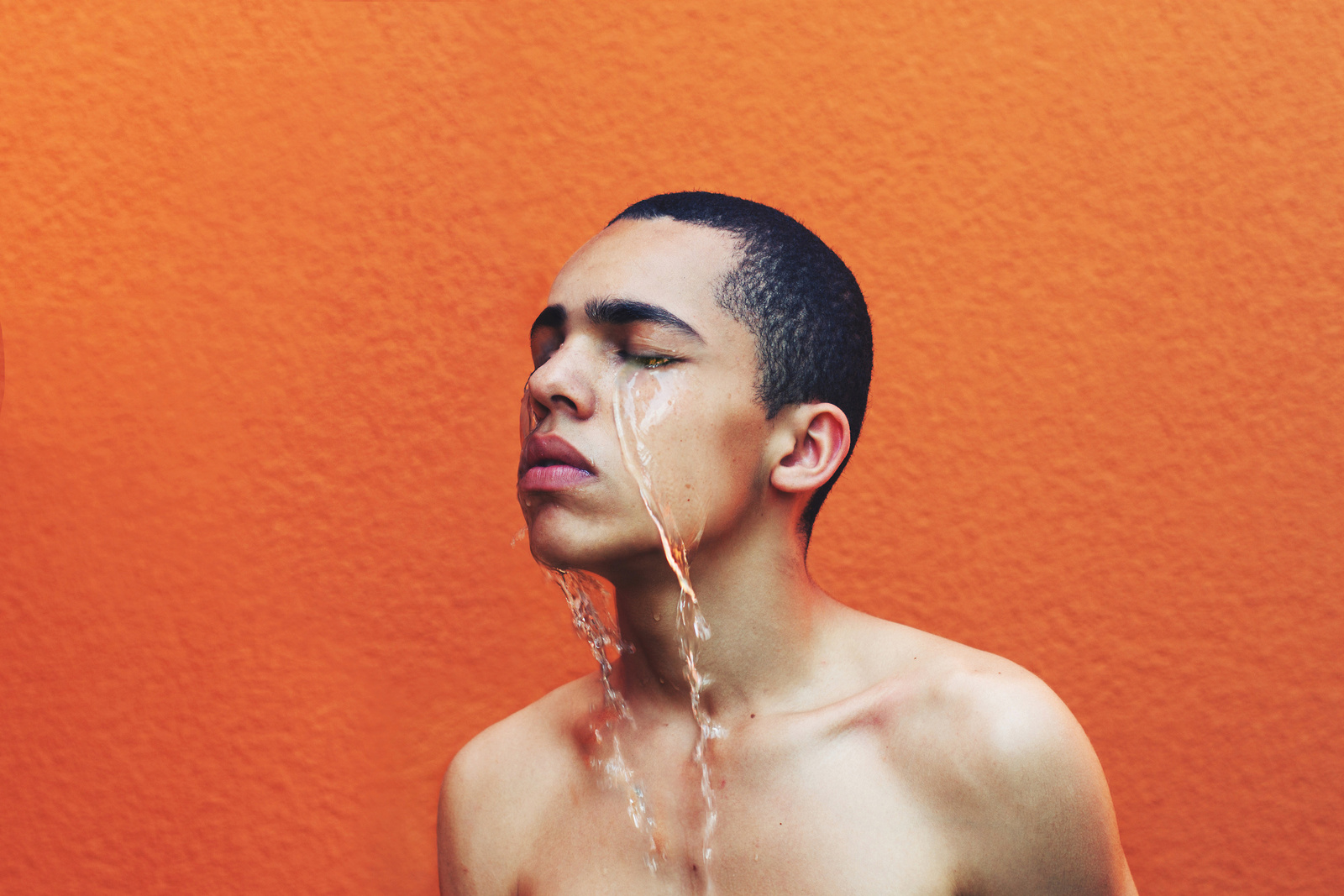 a young man is drinking water from a faucet