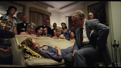 a group of people watching a man laying on a couch