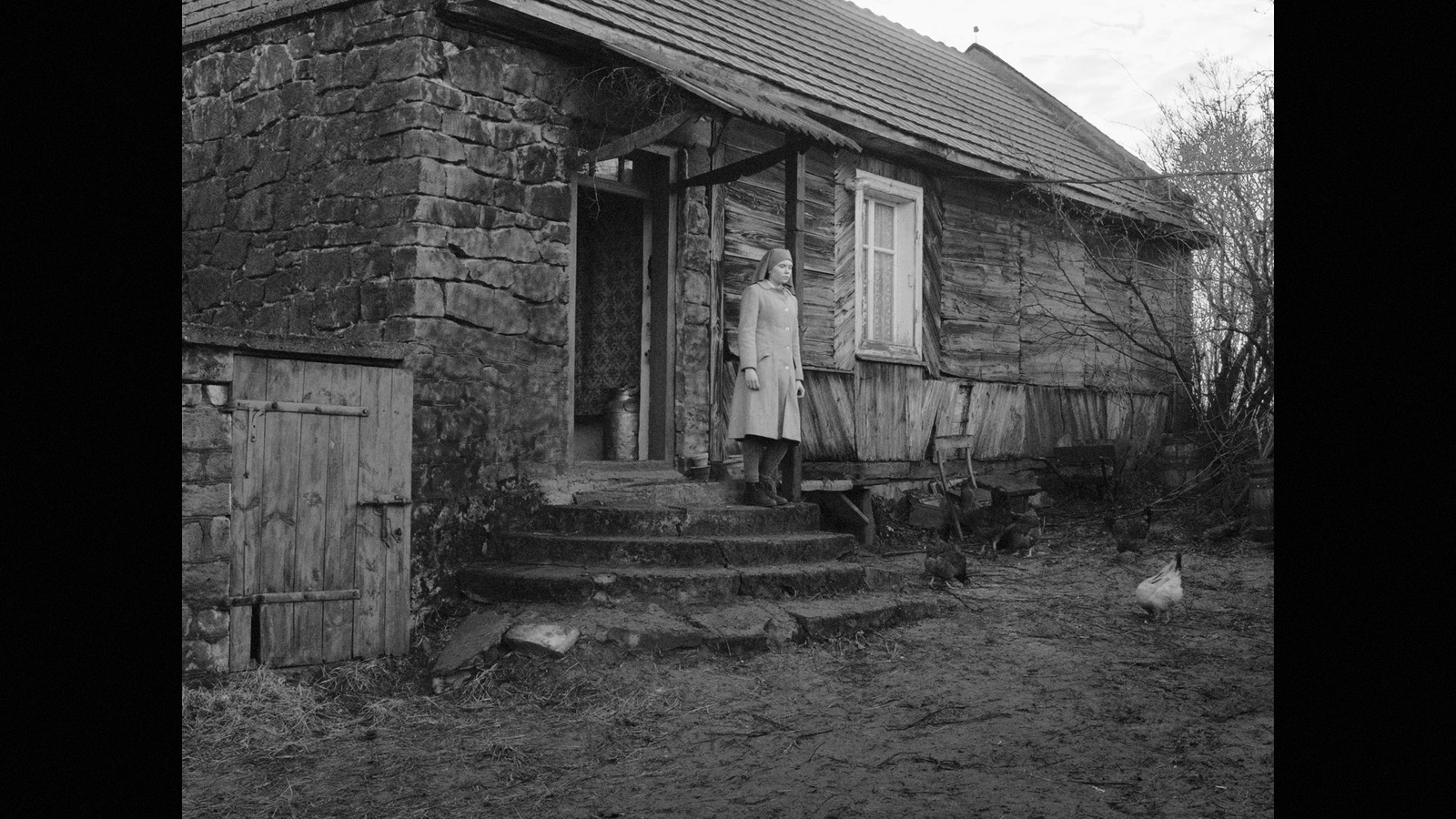 a black and white photo of a woman standing outside of a house