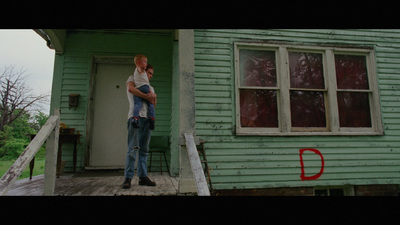 a man holding a child in front of a green house