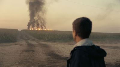 a man standing on a dirt road next to a field