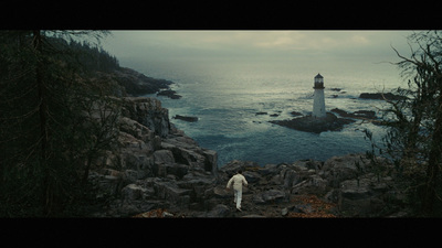 a man standing on a rocky cliff next to a lighthouse