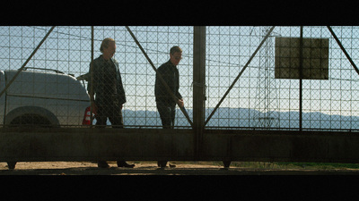 a couple of men standing next to each other behind a fence