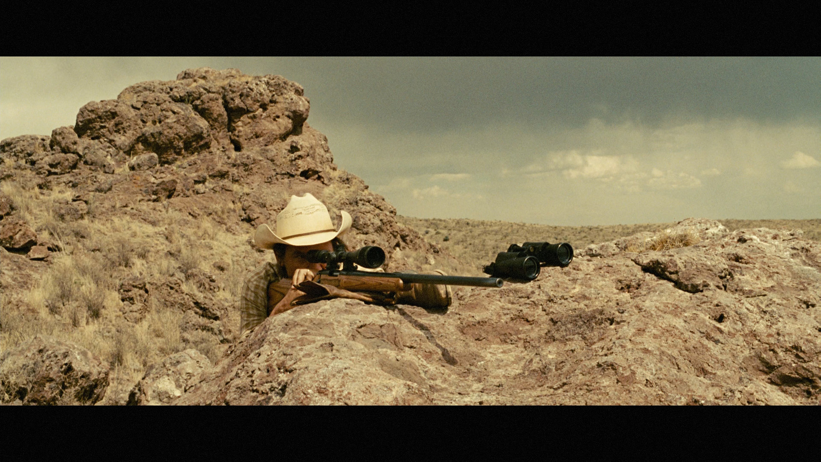 a man with a gun sitting on a rock