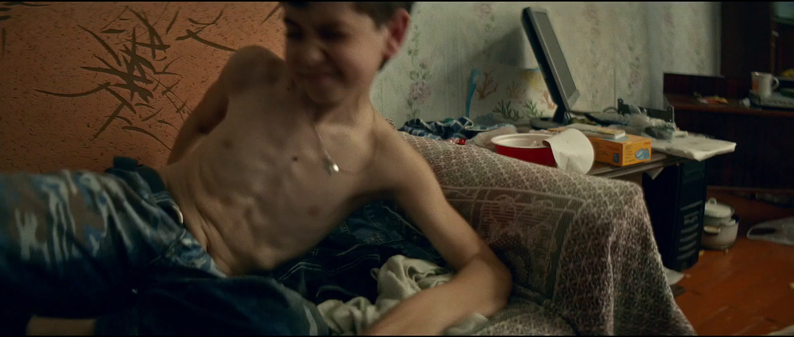 a shirtless man sitting on a bed in a messy room