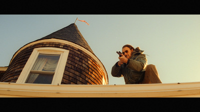 a man sitting on top of a roof pointing a gun