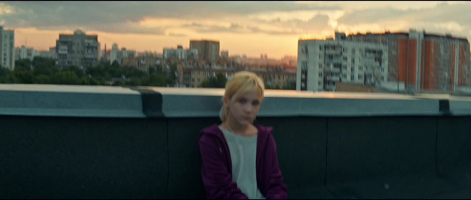 a woman sitting on top of a roof next to a tall building