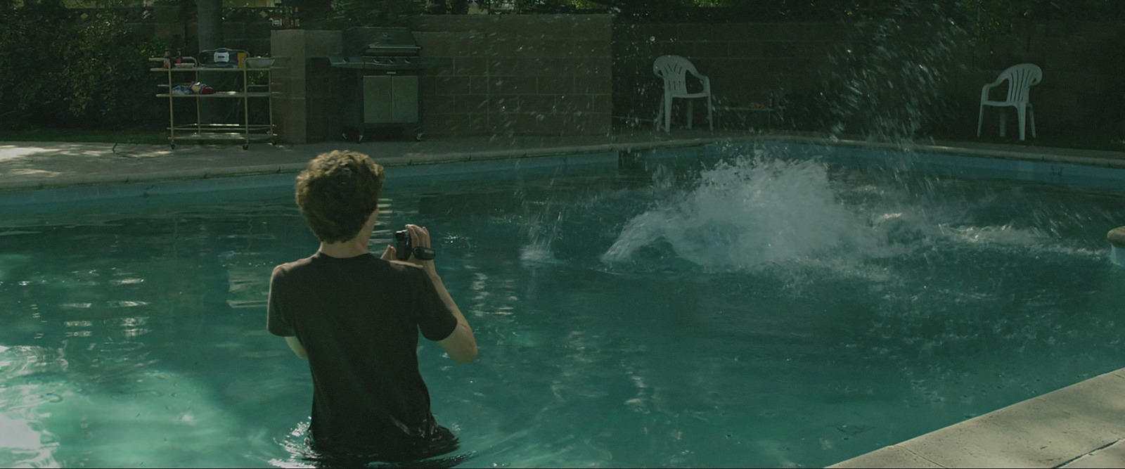 a boy taking a picture of a dolphin in a pool