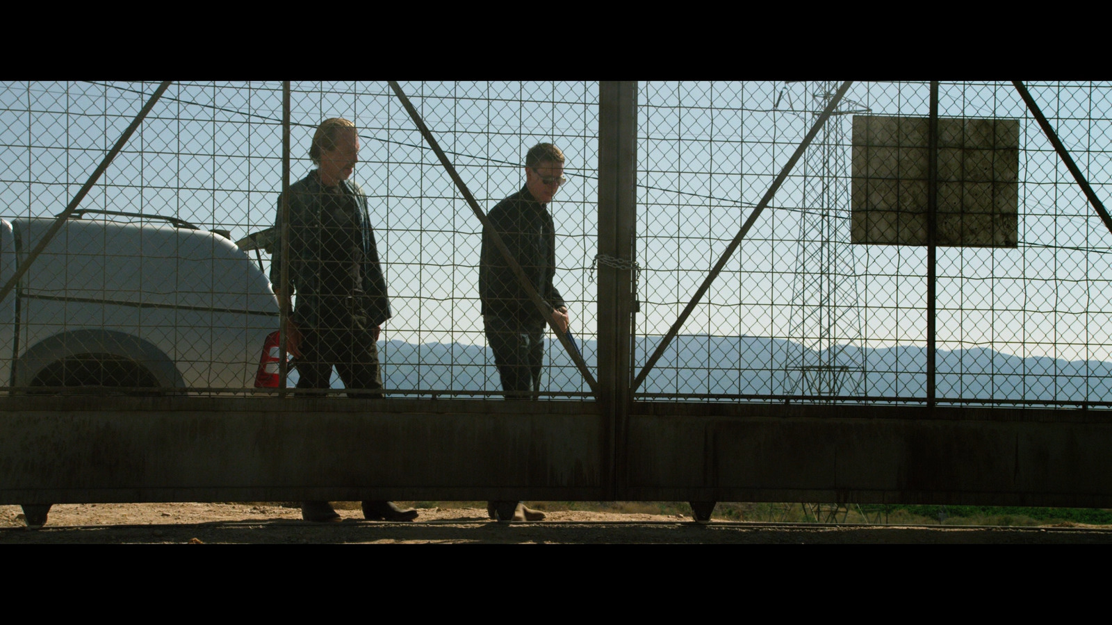 a couple of men standing next to each other behind a fence