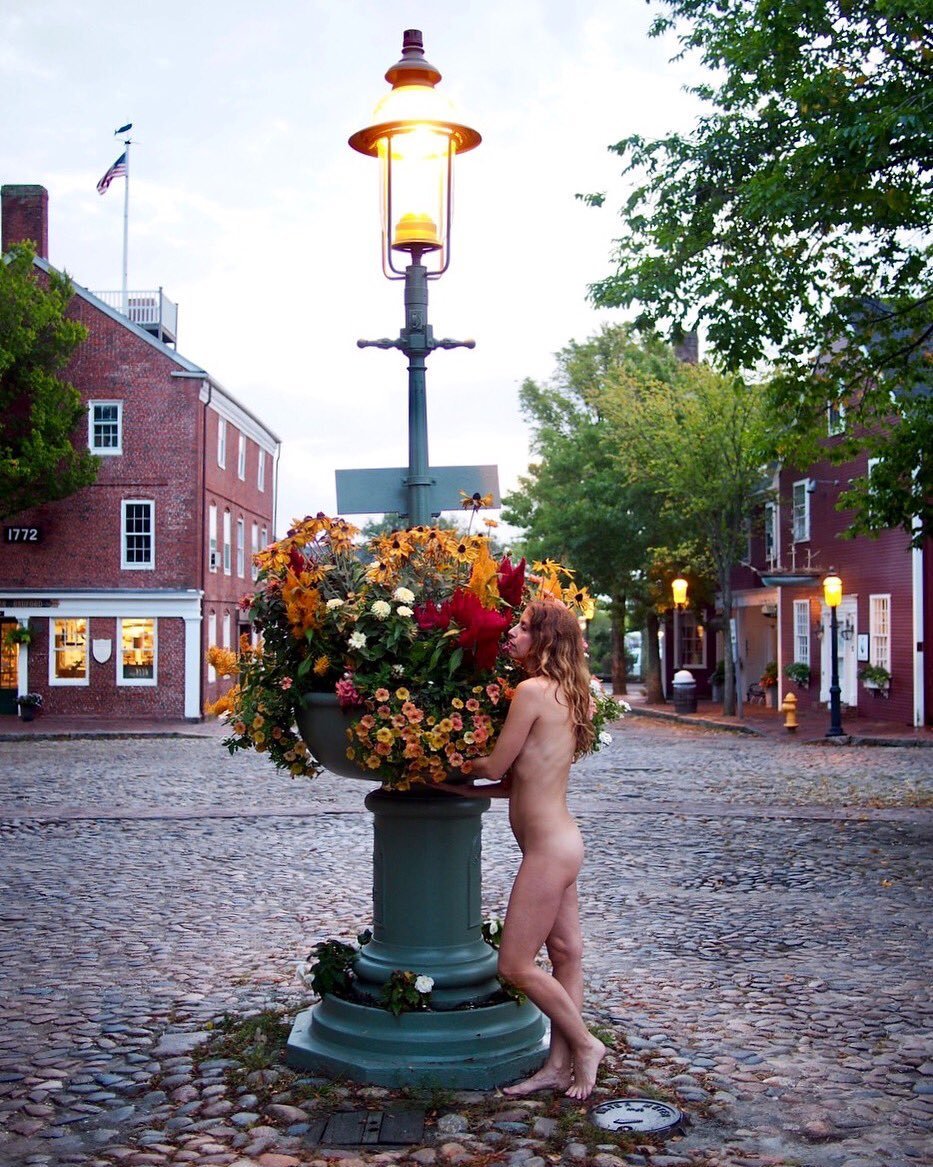 a naked woman standing next to a lamp post with flowers on it