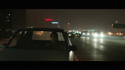 a woman in a car driving down a street at night