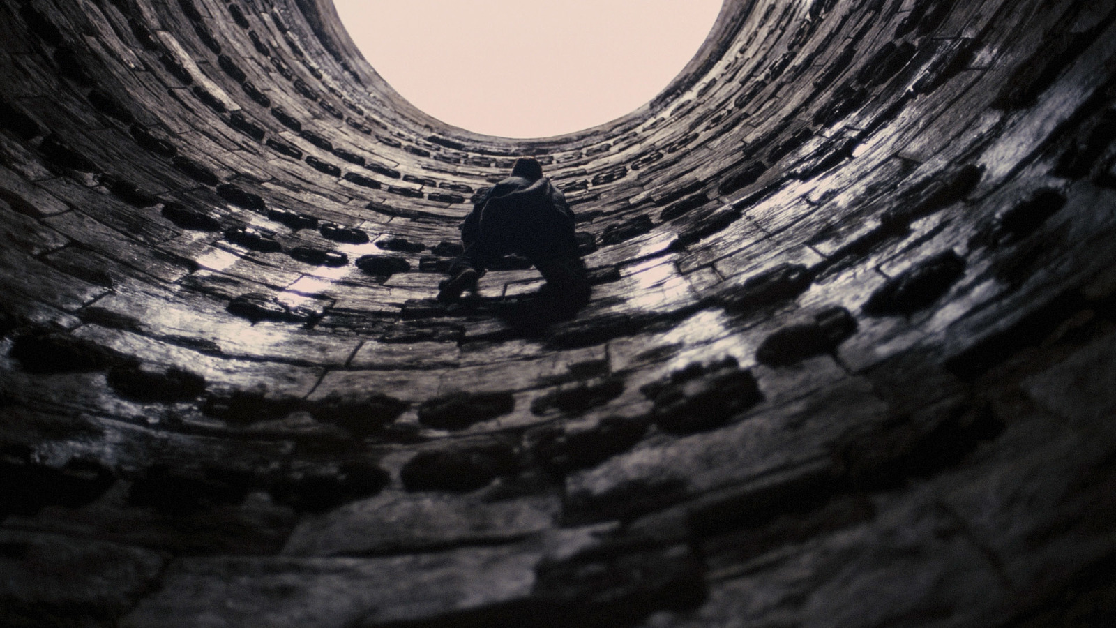 a man sitting in a stone tunnel with a sky background