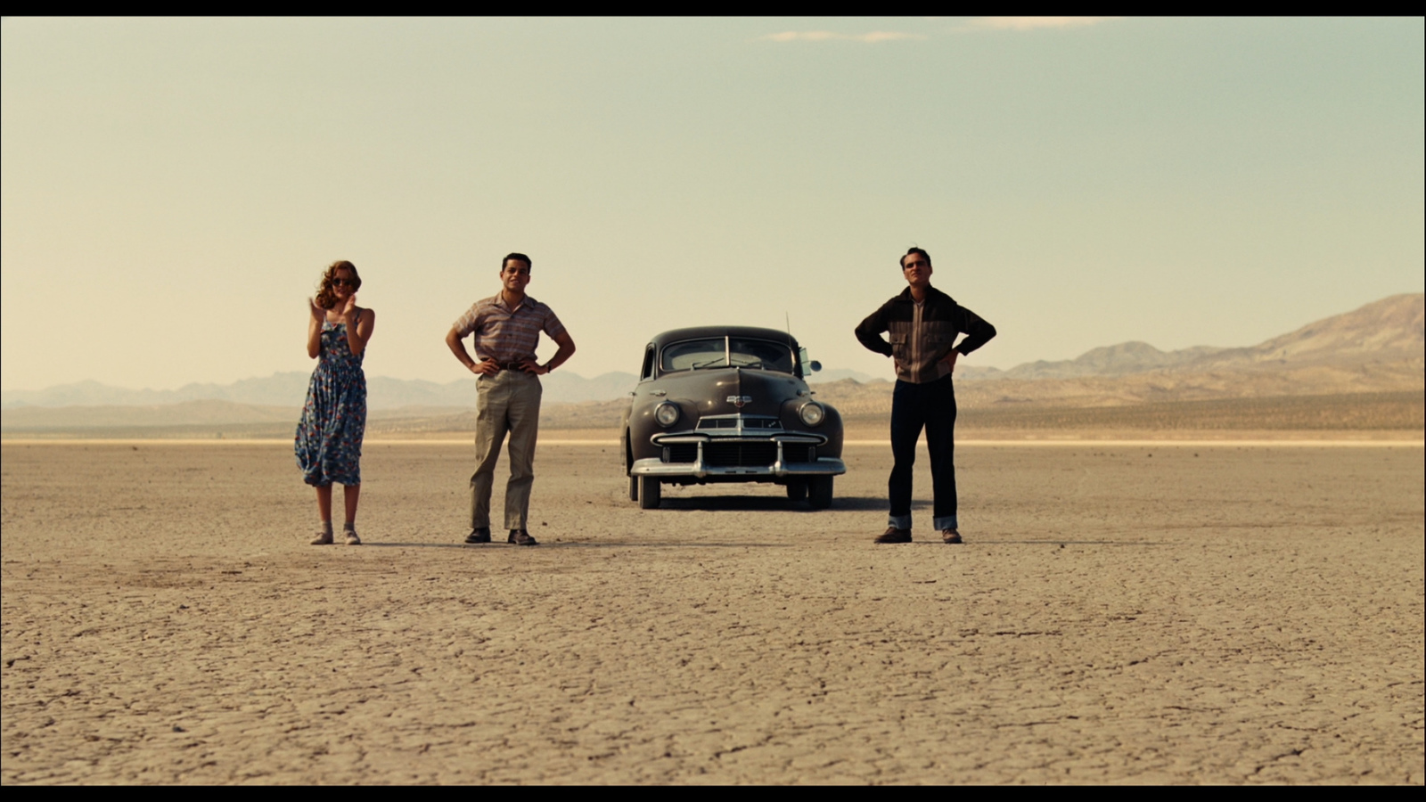 three people standing next to a car in the desert