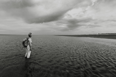 a black and white photo of a person walking in the water