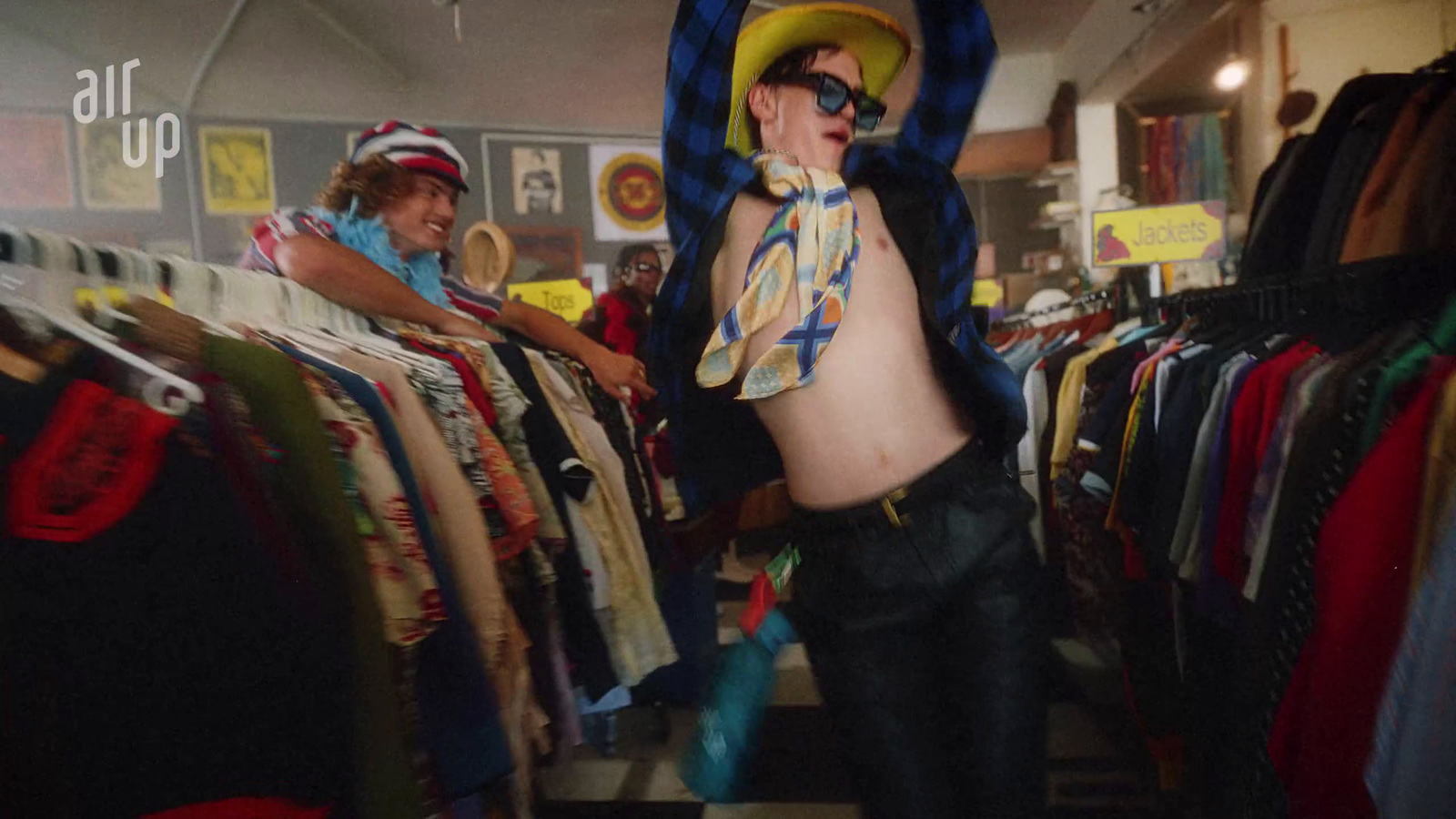 a man wearing a hat and sunglasses standing in front of a rack of shirts