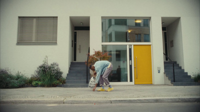 a woman walking down a street past a yellow door