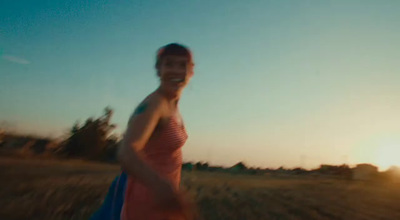 a woman walking through a field at sunset