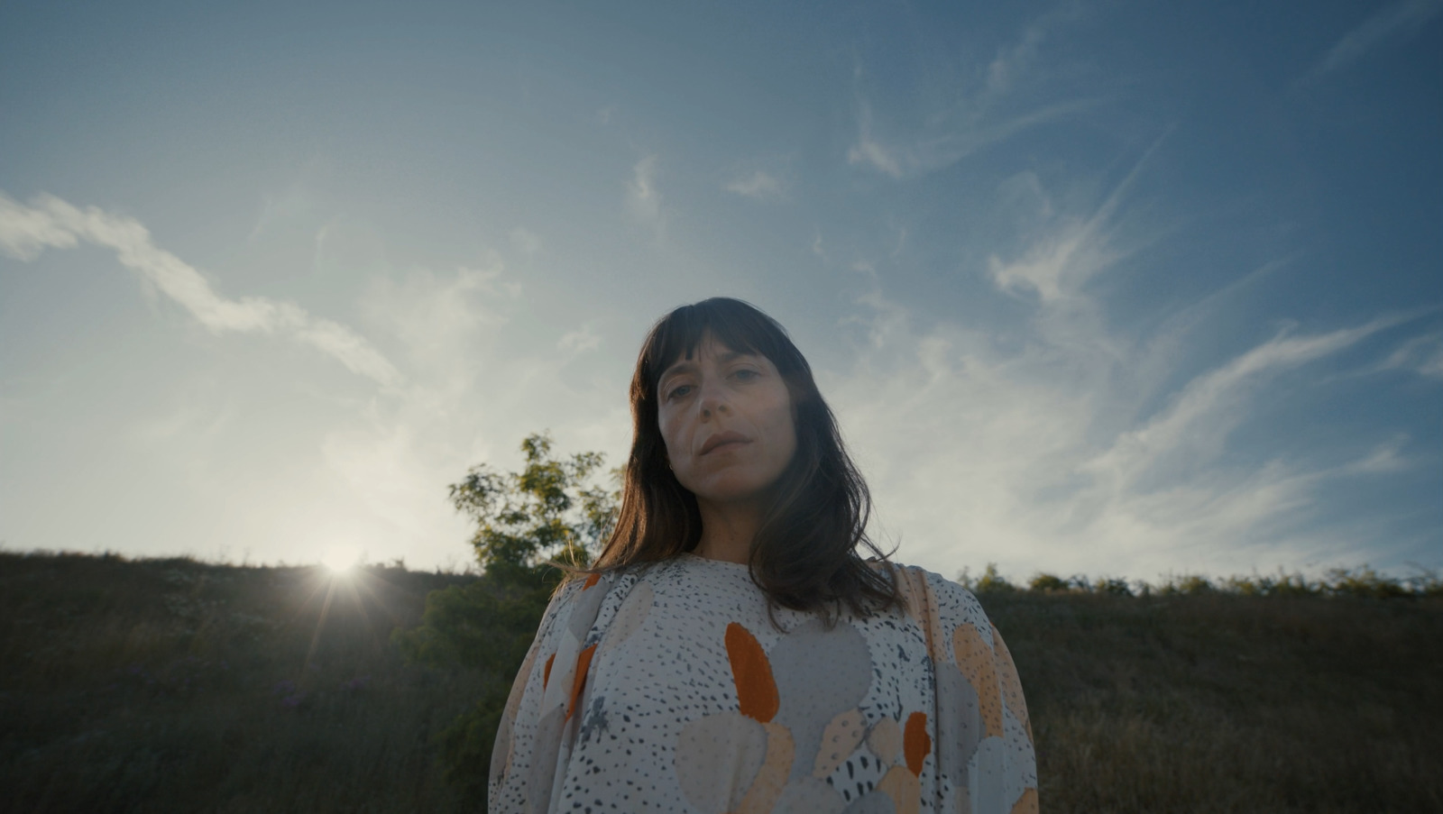 a woman standing in a field with the sun behind her