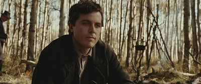 a man in a jacket and tie sitting in the woods