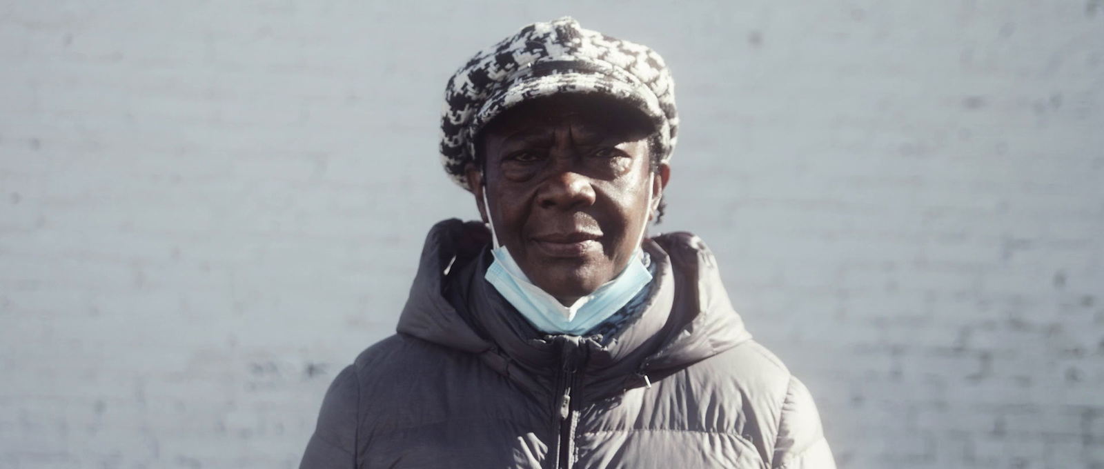 a man wearing a hat and jacket standing in front of a white wall