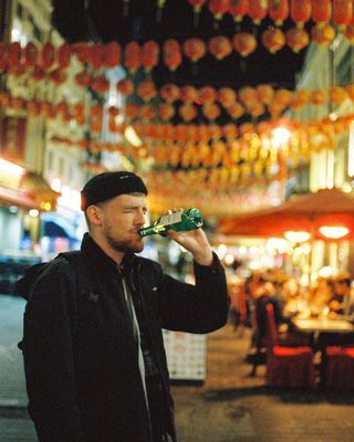 a man drinking from a green bottle in front of a restaurant