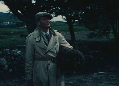 a man in a trench coat and hat holding a glove