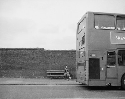 a man sitting on a bench next to a double decker bus