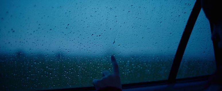 a person points at the rain outside of a window