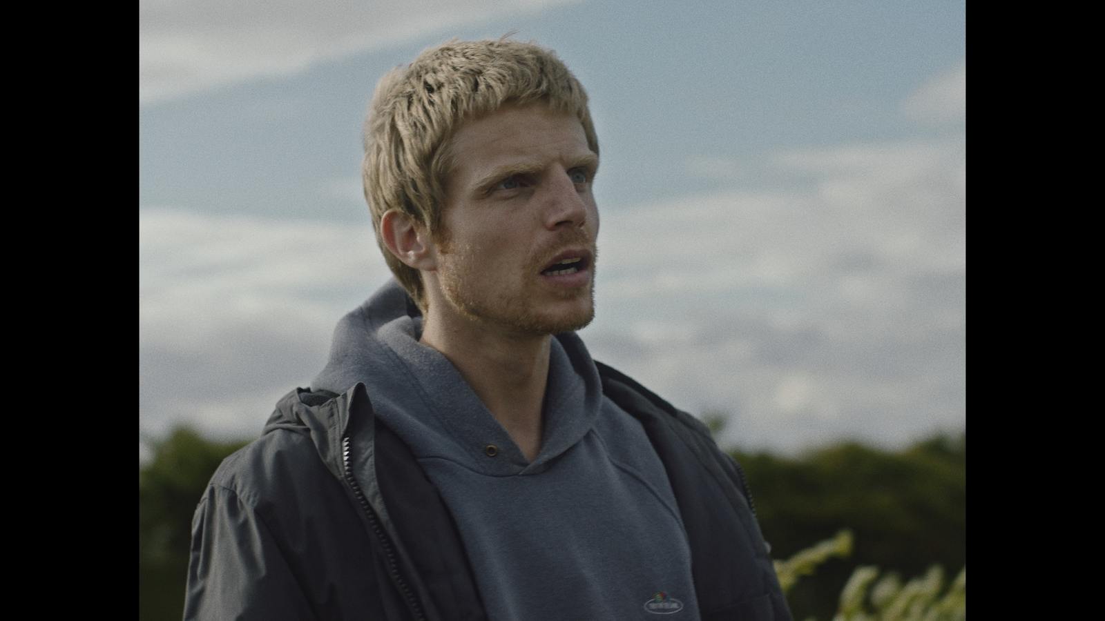 a man with blonde hair wearing a gray hoodie