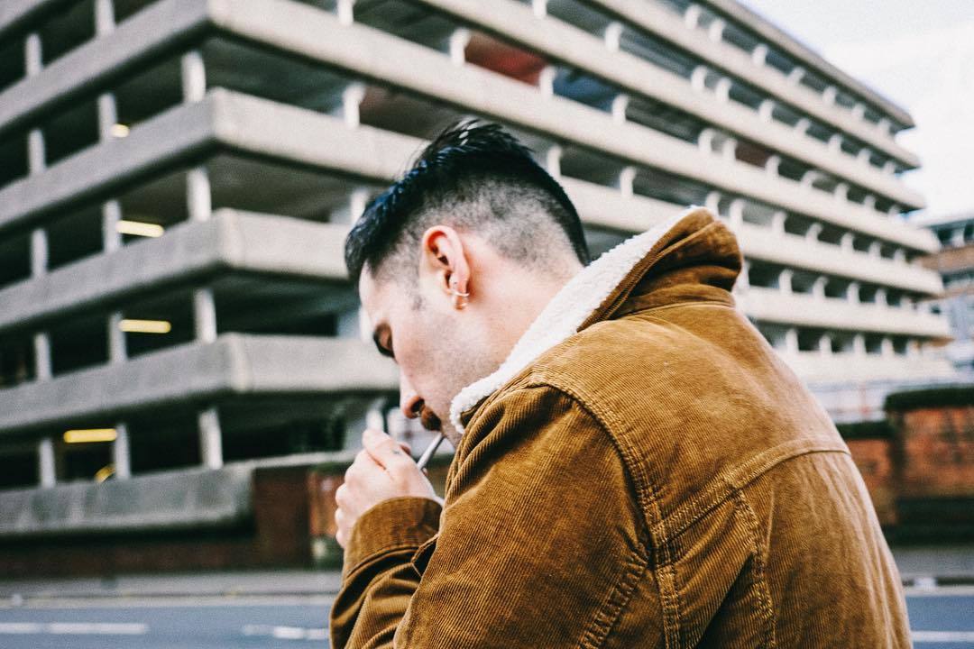 a man in a brown jacket smoking a cigarette