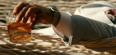 a man holding a glass of alcohol while sitting on a hammock