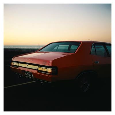 a red car parked in a parking lot next to the ocean