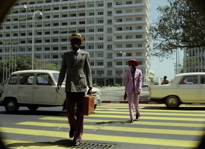 a man in a suit and hat walking across a street