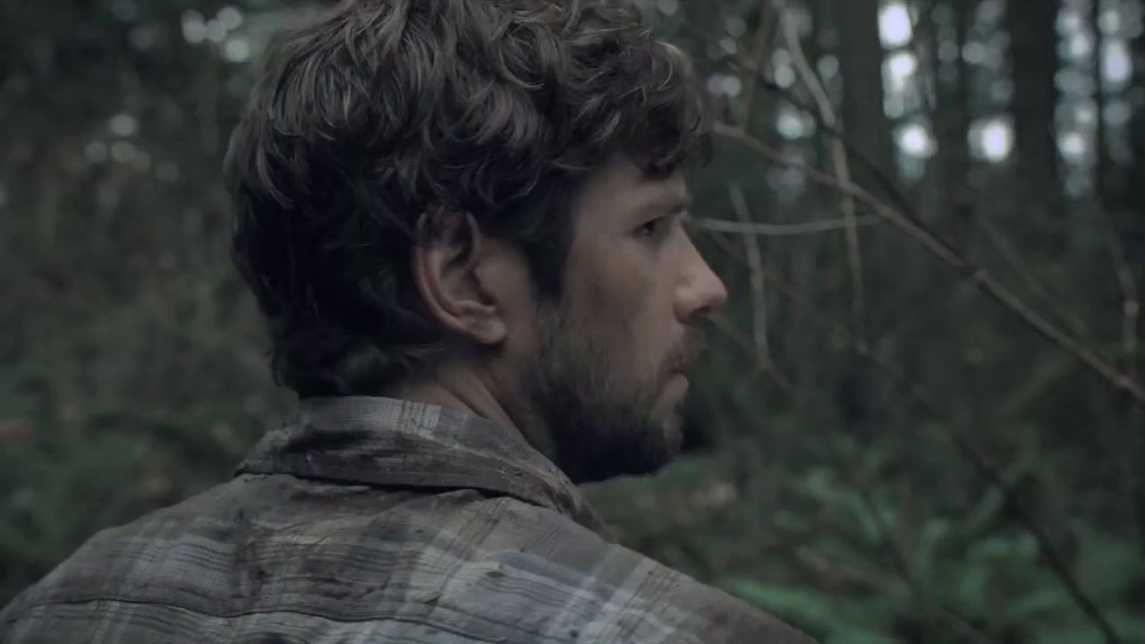 a man with a beard standing in the woods