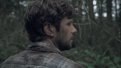 a man with a beard standing in the woods