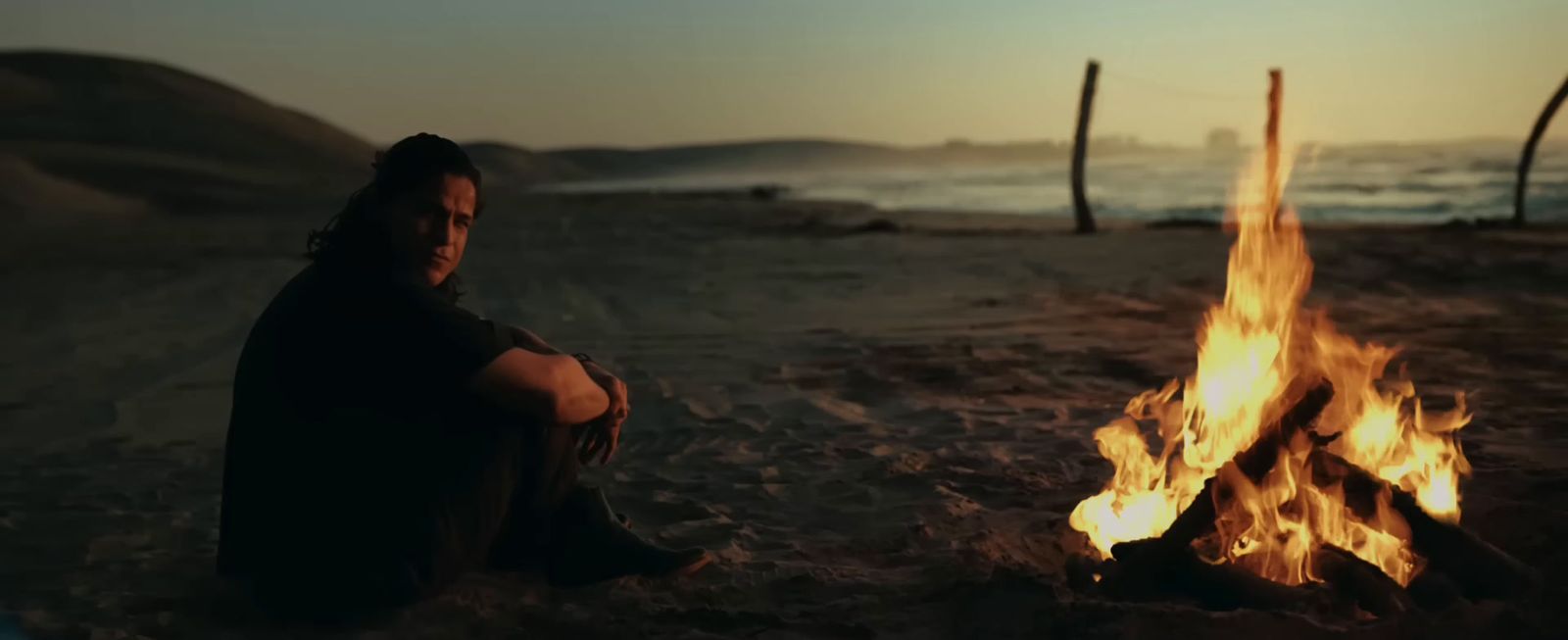 a man sitting in front of a fire on a beach