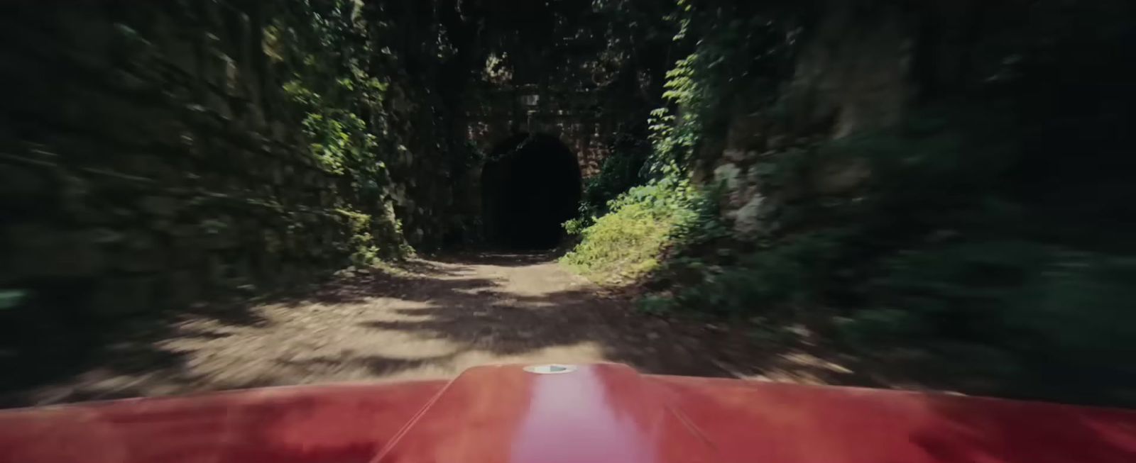 a red car driving through a tunnel in the woods