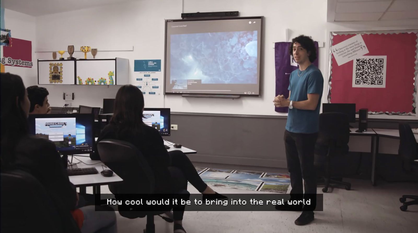 a man standing in front of a class room with a projector screen