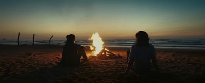 a couple of people sitting next to a fire on a beach